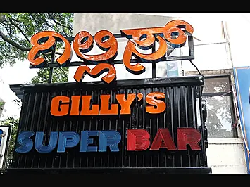 Illuminated orange and blue 3D letters for Gilly's Super Bar mounted on a black slatted storefront board