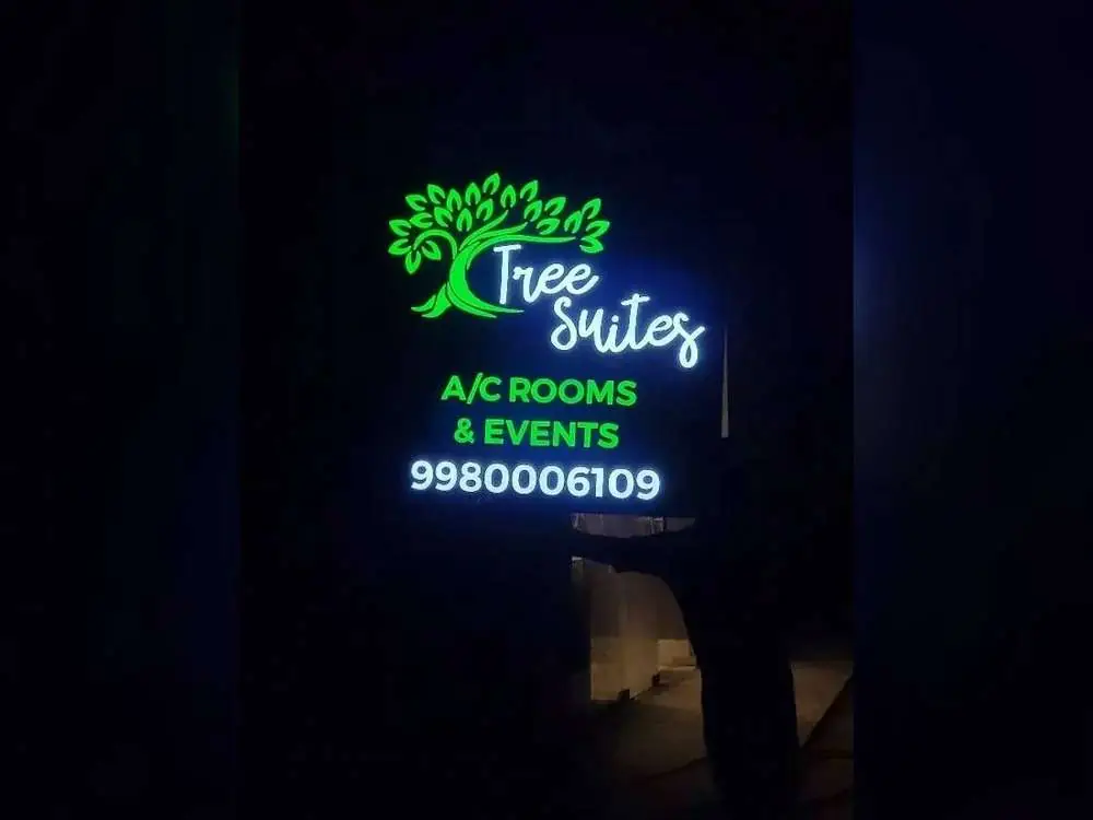 Backlit LED letter signage glowing green and blue at night for Tree Suites